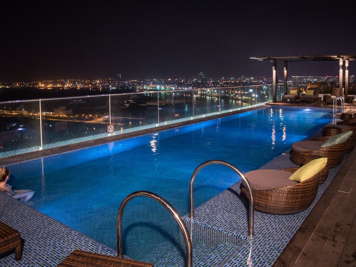 Rooftop pool lit up at night, with the lights of the river and the far bank