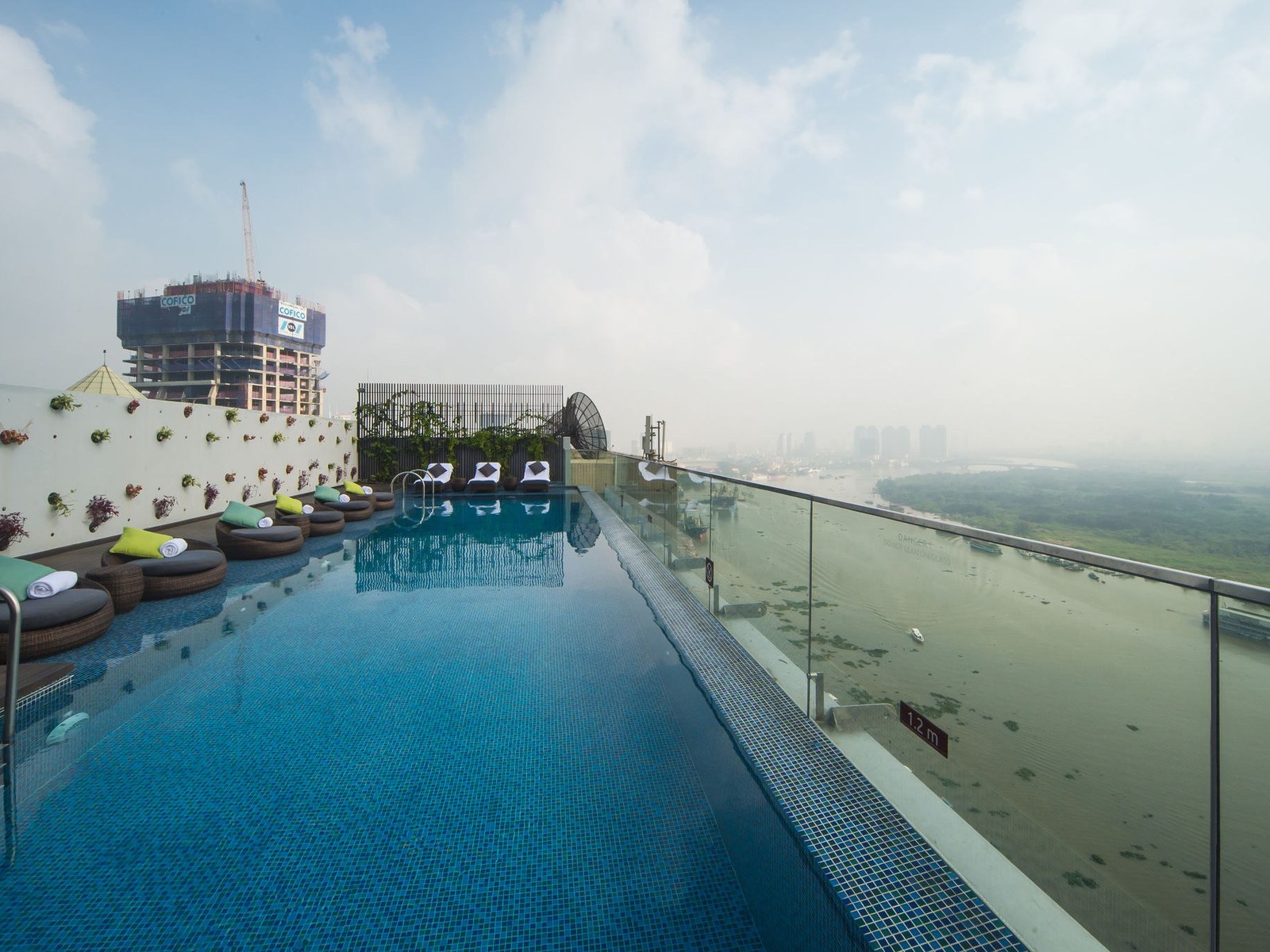 Rooftop infinity pool with cushioned loungers and the hazy bend of the river below