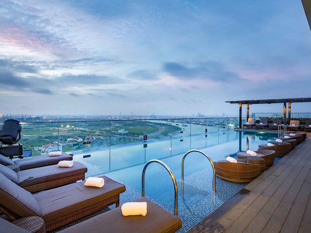 Rooftop infinity pool with sun loungers and the wide bend of the Saigon River at dusk
