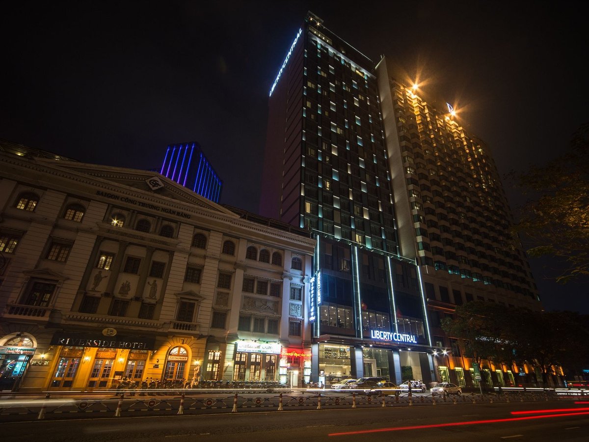 Hotel tower lit up at night beside an ornate colonial-era building on a riverside road