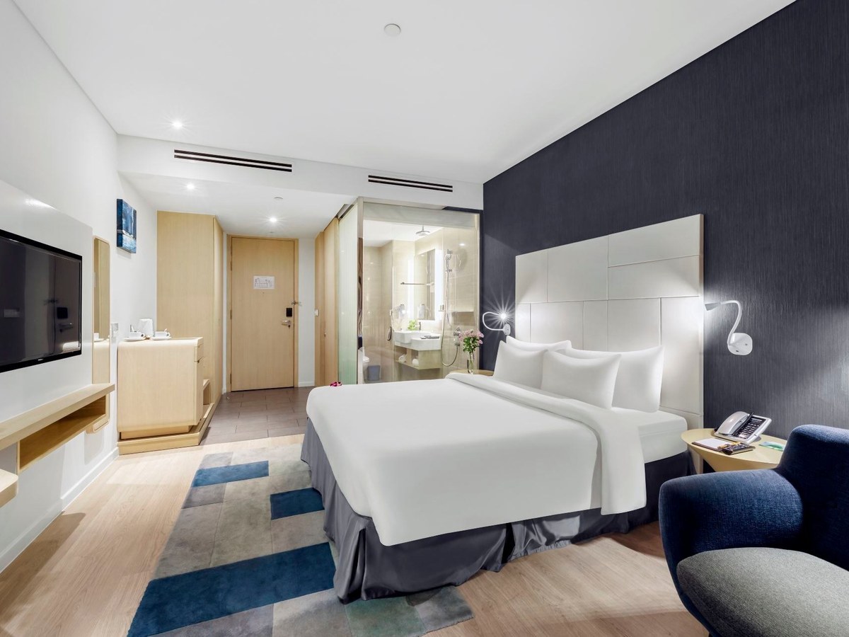 Compact hotel room with a king bed, a desk and a television on the wall