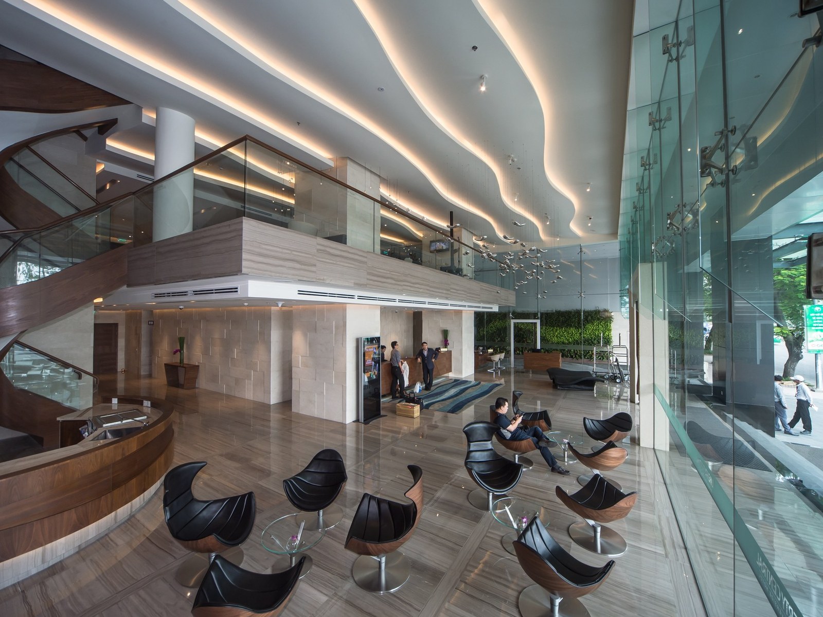 Hotel lobby with a curving staircase, polished floor and modern lounge chairs