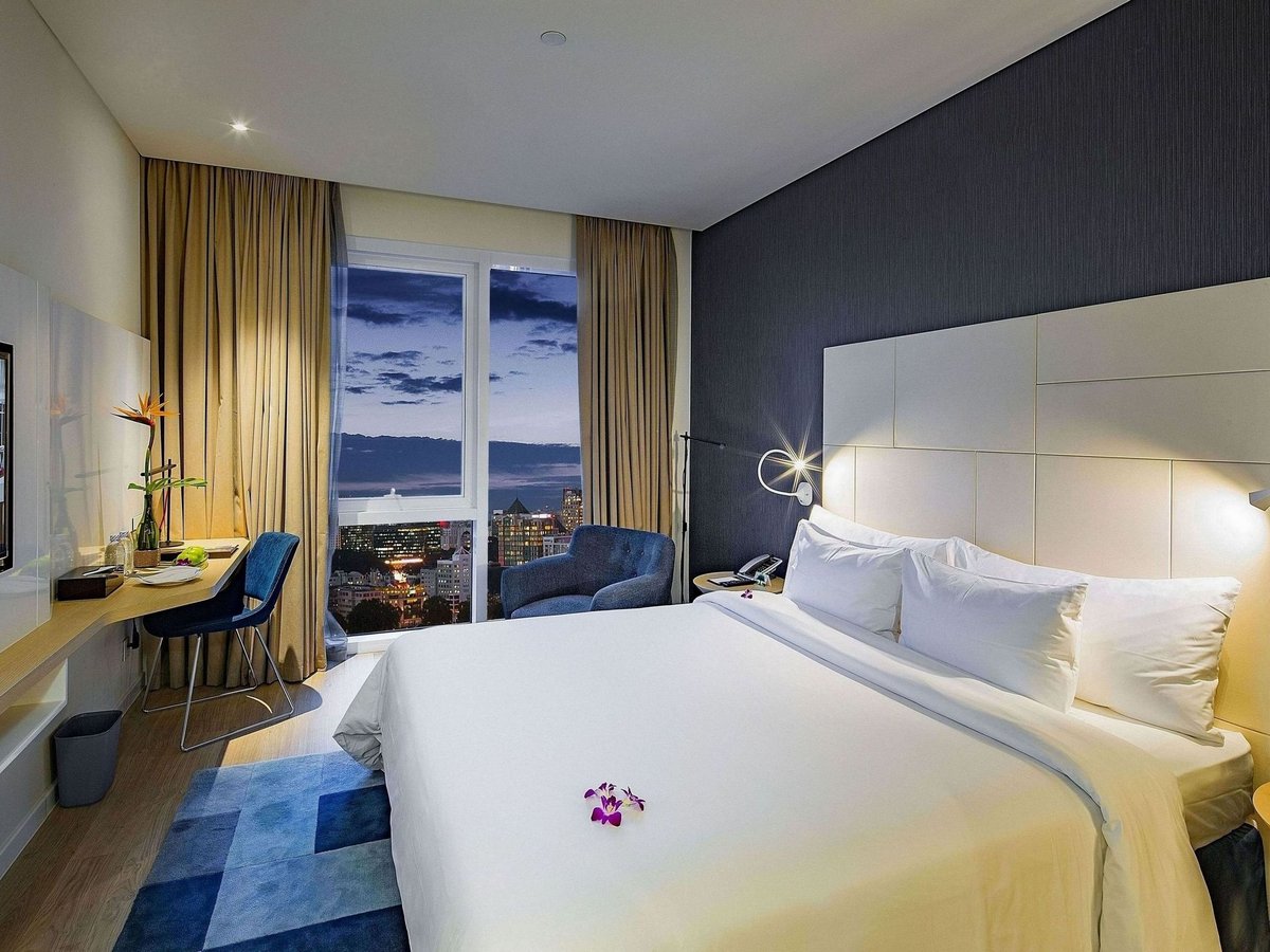 Deluxe room with a king bed, a desk and a window onto city towers