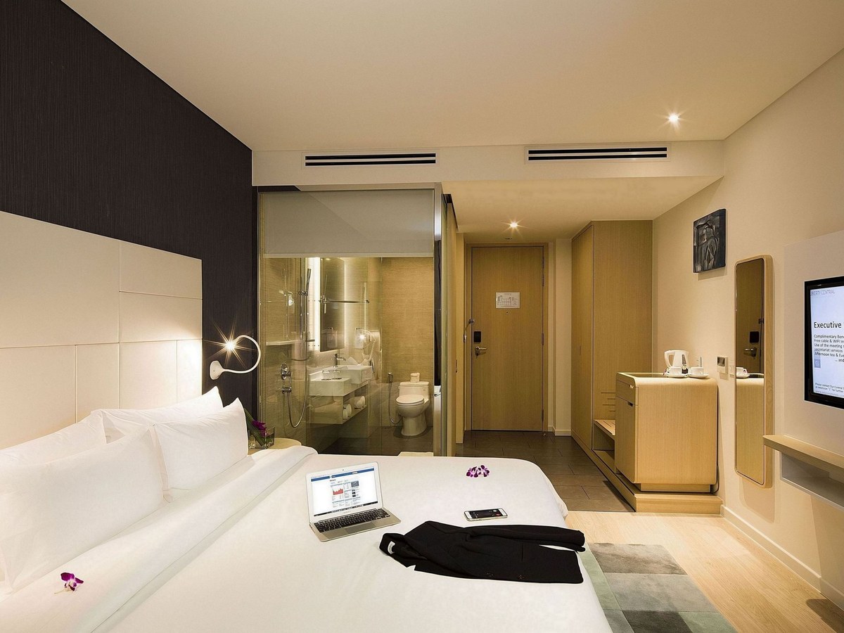 Executive room with a king bed, a laptop on the covers and a glass bathroom wall