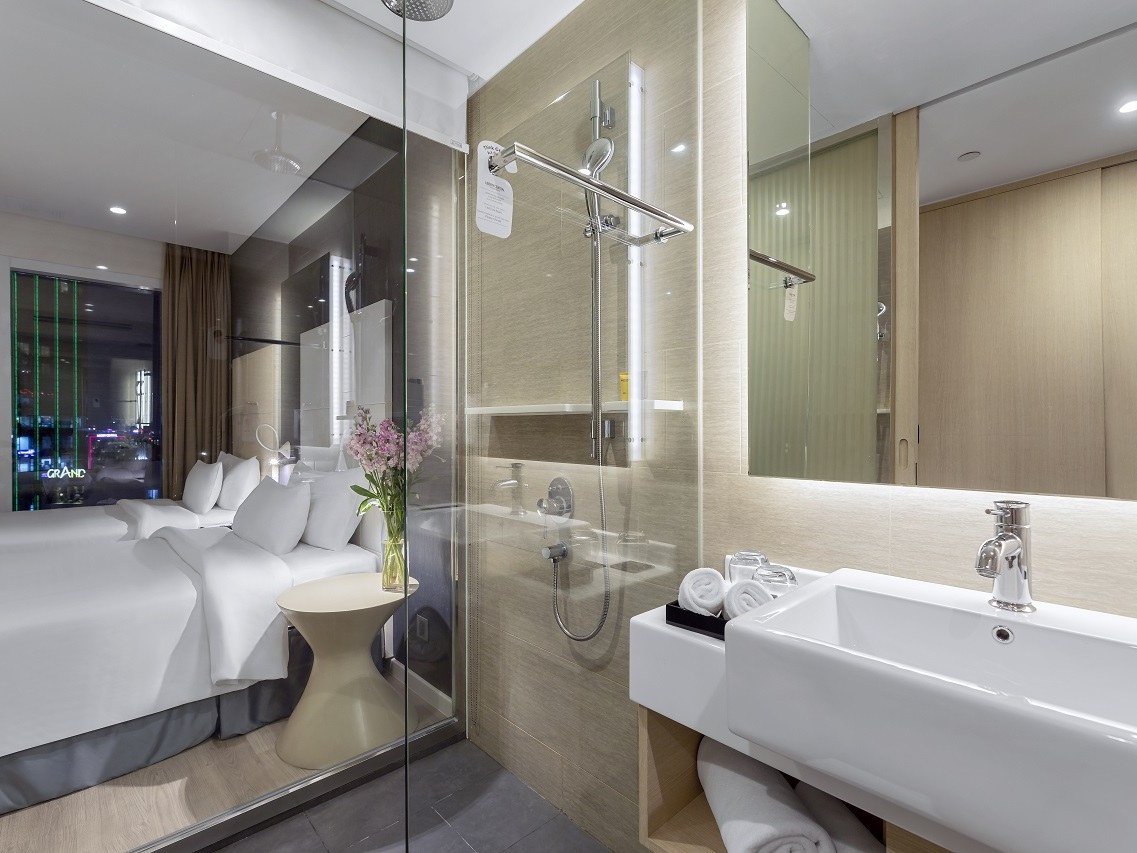 Room with a glass-walled shower beside the bed and a window onto the city